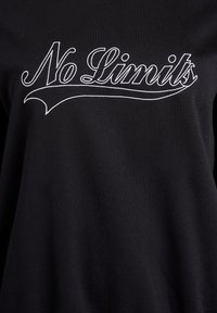 Black t-shirt made of soft fabric featuring white embroidered text that reads "No Limits" in a curved, dynamic font.