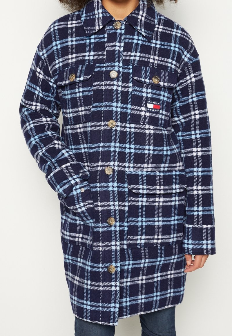 Cappotto a quadri in navy e azzurro chiaro realizzato in morbido tessuto, presenta due tasche frontali, chiusura con bottoni e un'etichetta con il logo del marchio sul petto.