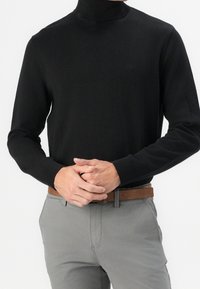 Zwarte coltrui gemaakt van een gladde, zachte stof. Heeft lange mouwen en een aansluitend ontwerp. Gecombineerd met lichtgrijze broek en een bruine riem.