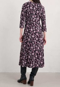 Czarna, zwiewna sukienka z różowym wzorem kwiatowym, z rękawami trzy czwarte i dopasowanym stanem, połączona z czarnymi, wysokimi na kolano, obcasami.