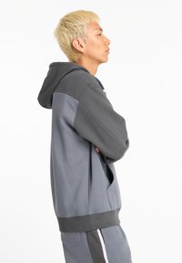 Sudadera gris con capucha y mangas de un gris más oscuro en contraste. Cuenta con un bolsillo frontal y un dobladillo acanalado. Textura suave y corte relajado.
