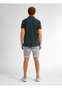 Donkergroen poloshirt met korte mouwen, eenvoudig ontwerp, gecombineerd met lichtgrijze korte broek met opgerolde zoom, gedragen met grijze sneakers.