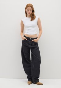 Top corto bianco a costine abbinato a jeans neri a gamba larga con vita alta. Presenta cuciture a contrasto e design a tasche piatte. Scarpe a punta marrone chiaro.