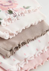 Zestaw trzech warstwowych bluzek z prążkowanej tkaniny w miękkim różu, beżu i bieli, z kwiatowymi wzorami i falistymi krawędziami.