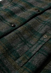 Wolljacke im grauen und grünen Karomuster, ausgestattet mit dunklen Knöpfen, einer strukturierten Oberfläche und einer Fronttasche mit geprägtem Logodesign.