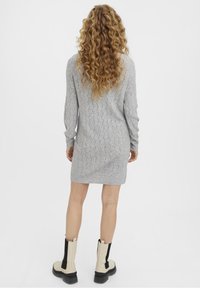 Robe tricotée grise avec un motif en vagues, manches longues, coupe décontractée et col rond, associée à des bottines beige et noires. 