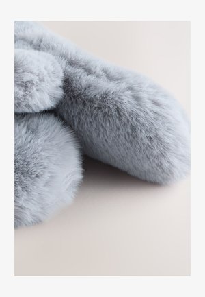 Tessuto in pelliccia sintetica grigia con una consistenza morbida e densa, caratterizzato da bordi soffici e arrotondati. Lo sfondo è chiaro e di tonalità neutra.