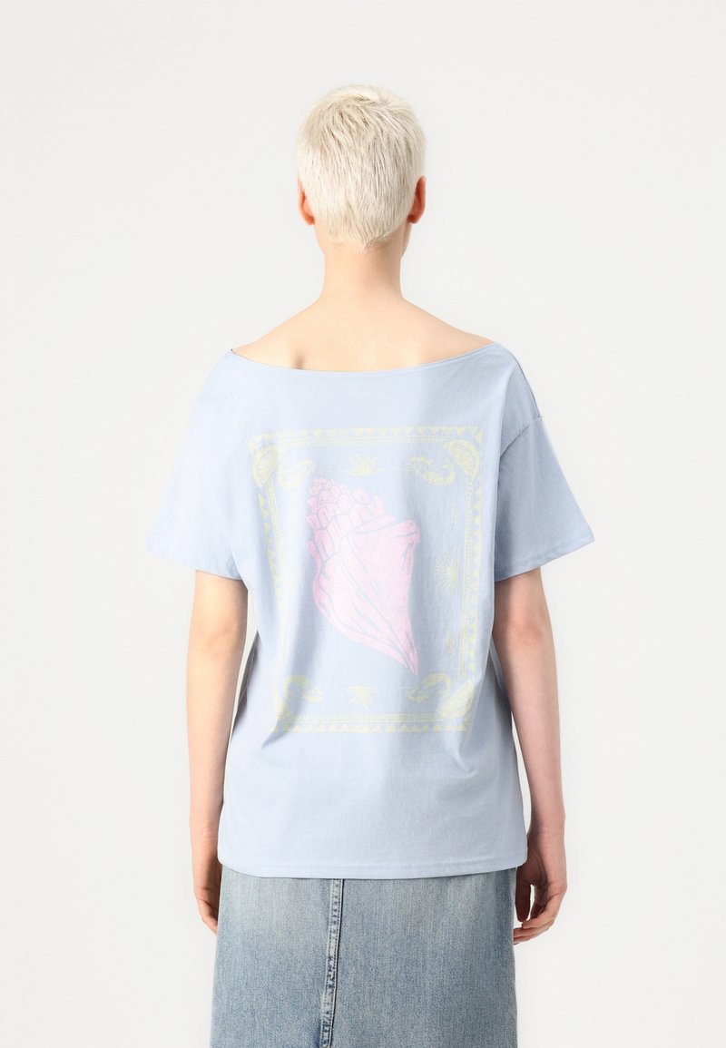 Světle modré oversize tričko s širokým výstřihem, na zadní straně s grafikou růžové mušle uvnitř žlutého rámečku. Měkký bavlněný materiál.