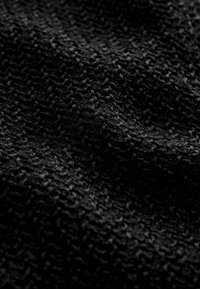 Tissu noir texturé présentant un petit motif en relief, créant une surface tactile avec profondeur et variation dans la réflexion de la lumière.