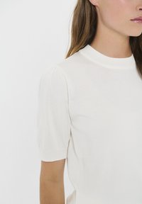 White short-sleeve knit top with a high neck, featuring a textured finish and subtle puffed shoulder detailing.