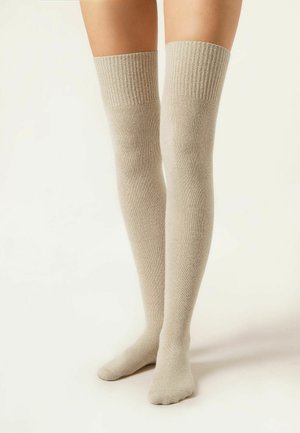 Chaussettes beiges arrivant au genou, en tissu doux, avec un haut côtelé. Texture lisse et forme ajustée, recouvrant la jambe au-dessus du genou.