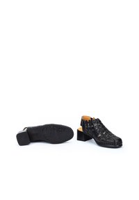 Chaussures ouvertes en cuir noir avec un design supérieur tissé, un petit talon bloc et une semelle texturée, mettant en valeur des détails complexes et une finition lisse.