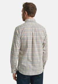 Tjekket skjorte i beige, blå og brune farver. Har knap-ned krave, lange ærmer og en rund kant. Stoffet ser letvægts ud.