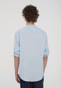 Camicia a maniche lunghe blu chiaro con colletto a punta, maniche arrotolate e orlo curvo. Tessuto morbido con una texture liscia.