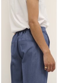 Pantalon en denim à coupe décontractée, avec un tissu bleu foncé texturé, une taille élastique et deux poches arrière plates.