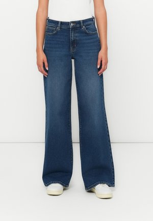 Vidde ben denim jeans i mørkeblå med høy midje, fem lommer og subtile stikninger. Kombinert med hvite joggesko.