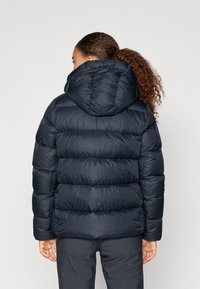 Tumesinine puffer-jakk, millel on kapuuts, omab kurrulist disaini, elastseid mansette ja siledat läikivat viimistlust. Tagakülg näitab täidlast ja kuju.