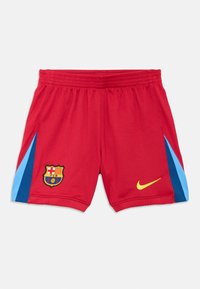 Pantaloni scurți de fotbal roșii cu accente laterale bleu și bleumarin, având un logo Nike galben și blazonul încrustat al Barcelonei pe partea din față.