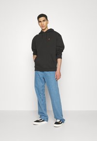 Sudadera negra con capucha y bolsillo tipo canguro, combinada con jeans azul claro y zapatillas negras con suelas blancas.