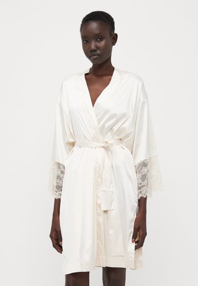 Accappatoio di seta di un avorio chiaro con maniche bordate in pizzo, dotato di una vita con cintura e una finitura in raso morbido. Design elegante e vestibilità ampia.