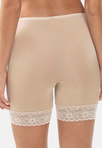Beige mid-thigh-långa formande shorts för kvinnor med spetsdetaljer, visas bakifrån på en stående modell.
