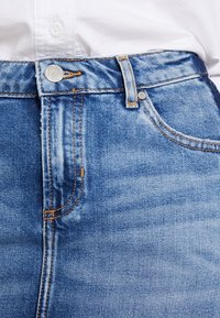 High-waisted blue denim jeans with a slight fade, contrast stitching, and a metal button closure at the waist.