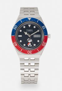 Zegarek automatyczny Timex z granatową tarczą, stalową bransoletą, czerwono-niebieską lunetą, zawierający ilustrację Snoopy, wyświetlacz daty oraz odporność na wodę.