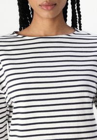 Czarny i biały pasiaste bluzka z miękkiego materiału, z dekoltem w łódkę i luźnym krojem. Pasy są równomiernie rozmieszczone i poziome.
