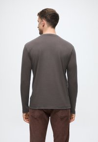 Tamsiai pilkas ilgomis rankovėmis marškinėliai, pagaminti iš minkštos medžiagos. Suapvalintas iškirpimas ir šiek tiek prigludęs kirpimas. Derinami su rudo veliūro kelnėmis.