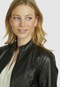 Black leather jacket with a high collar, featuring a fitted design and subtle stitching details. Zipper closure and smooth texture.
