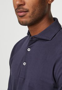 Marineblaue Polohemd aus Baumwolle, mit einer Knopfleiste mit silbernen Knöpfen, gefaltetem Kragen und glatter Textur.