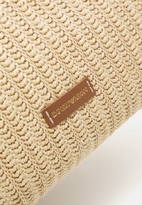 Vävd halmhandväska i beige med ett strukturerat mönster. Har en brun läderetikett präglad med "EMPORIO ARMANI" i guld.