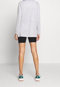 Maglia grigia a maniche lunghe con un taglio morbido, abbinata a pantaloni corto da ciclismo neri e scarpe da ginnastica multicolori con un dettaglio rotondo nel tallone.