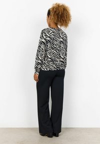 Black and beige zebra-striped long-sleeve top paired with black wide-leg pants. The fabric appears smooth with a relaxed fit and round neckline.