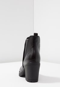 Schwarze Leder-Ankle Boots mit strukturierter Oberfläche, dreieckigem Absatz, elastischen Seitenpaneelen und einer Zuglasche für einfaches Anziehen.