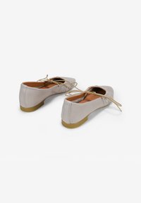 Bailarinas de cuero color beige claro con punteras redondeadas y suelas de goma pequeñas y flexibles. Cuentan con cordones y una textura suave.