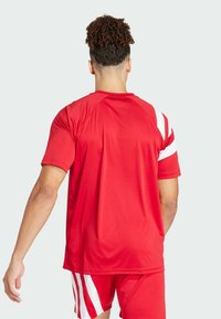 Rotes Sportshirt mit kurzen Ärmeln und weißen Streifen auf den Schultern. Weicher, leichter Stoff mit lockerer Passform.