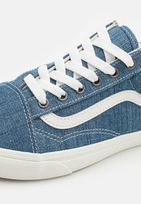 Sneaker din denim cu o parte superioară din material albastru, șireturi albe, ochiuri din metal și talpa din cauciuc gri. Prezintă o dunga albă clasică pe lateral și detalii cusute.