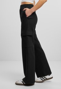 Schwarze Cargo-Sweatpants mit weitem Bein, ausgestattet mit Seitentaschen und einem gerippten Bund, hergestellt aus einem weichen Baumwollmischgewebe.