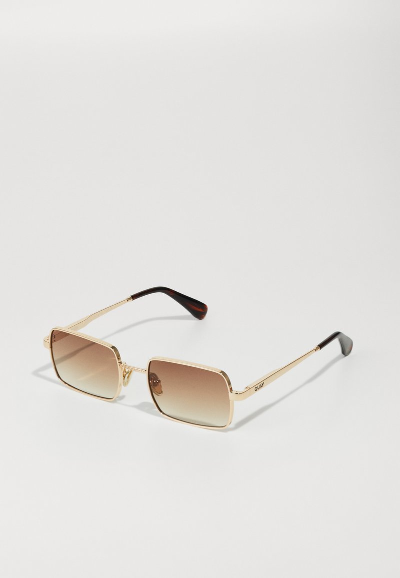 Lunettes de soleil dorées avec des montures carrées, des verres dégradés brun et des accents écaille de tortue sur les branches. Design en métal léger.