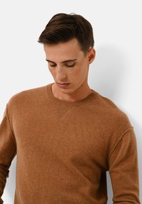 Brauner Strickpullover aus weichem Material; verfügt über einen runden Halsausschnitt und eine feine Struktur; sichtbare genähte Details am Kragen und den Nähten.