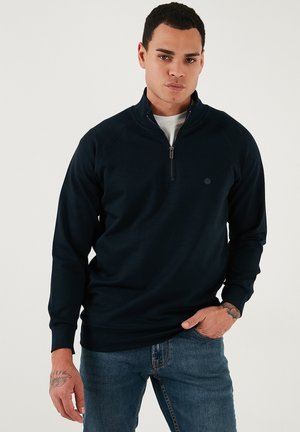 Marineblå fleece-pullover med kvart-lynlås krave og raglanærmer. Den har et lille logo på brystet og ribbede manchetter.