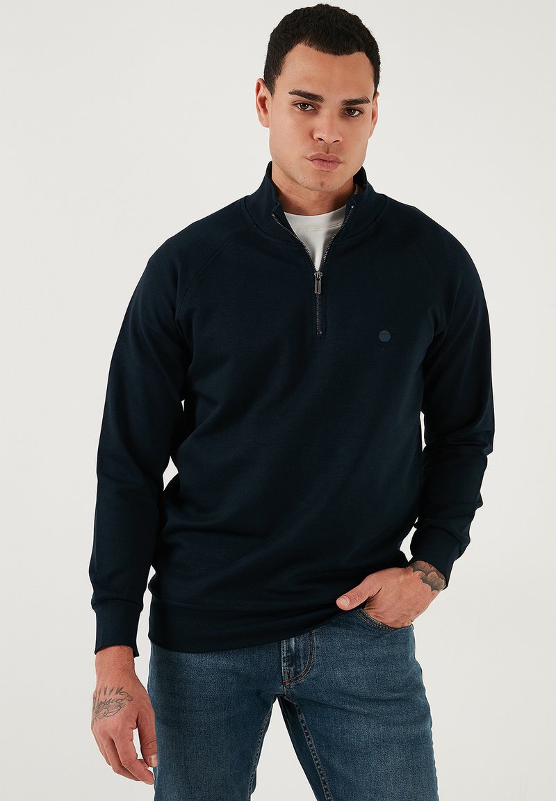Tengerészeti kék polár pulóver negyed zippel, és raglán ujjal. A mellrészen egy kicsi logó található, valamint bordázott mandzsetták.