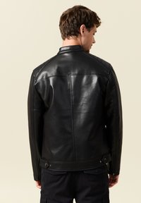 Giacca da moto in pelle nera con accenti a spalla trapuntati e colletto aderente, caratterizzata da una texture liscia e una silhouette aderente.