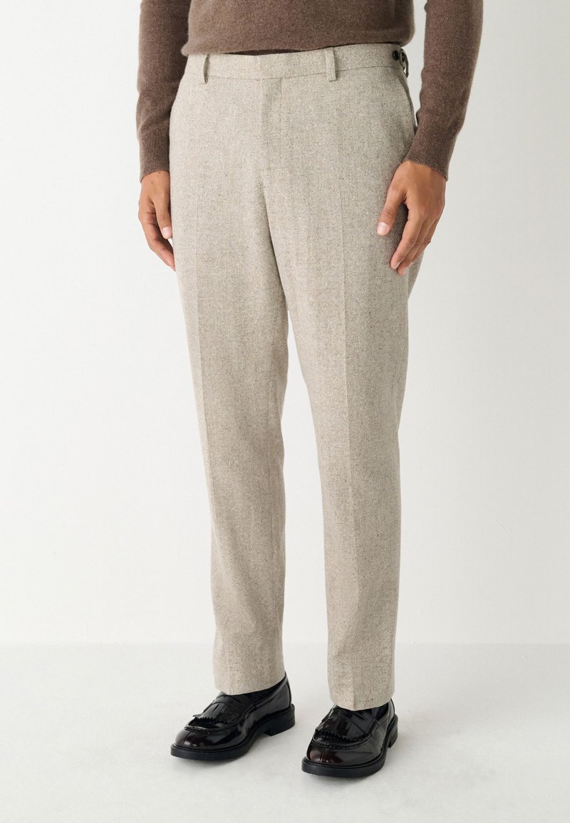 Pantalon beige sur mesure en tissu texturé, doté d'un devant plat, de poches latérales et d'une fermeture à deux boutons à la taille.
