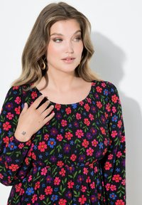 Czarna sukienka w kwiaty z żywymi różowymi, niebieskimi i zielonymi motywami. Posiada okrągły dekolt, marszczoną teksturę i długie rękawy.