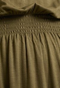 Tissu vert olive avec une ceinture élastiquée froncée formant de petits plis espacés uniformément sous la bande.