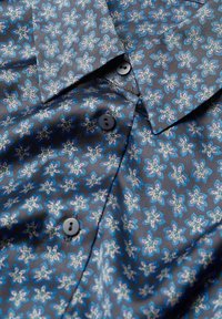 Camicia blu scuro con un motivo ripetuto di piccoli motivi floreali azzurri e beige, bottoni neri e colletto a punta.