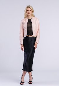 Lichtroze leren cropped jack met een ronde halslijn, gecombineerd met een zwarte satijnen rok en zwarte hakken met bandjes. Glad materiaal, getailleerde pasvorm.