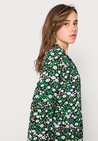 Vestido preto floral com um padrão de flores brancas, rosas e verdes. Mangas longas e um corte solto com um design de cintura ligeiramente franzida.